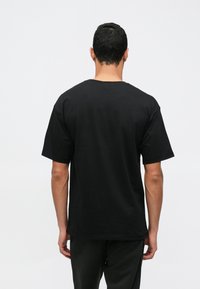 Μαύρο βαμβακερό T-shirt με κλασικό λαιμό και κοντά μ�ανίκια, με απλή σχεδίαση στην πλάτη χωρίς ορατά λογότυπα ή μοτίβα.