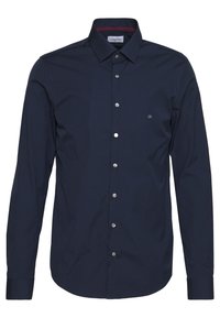 Camisa de manga larga azul marino hecha de una mezcla de algodón. Cuenta con un cuello abotonado, botones plateados y un pequeño logo de CK en el pecho.