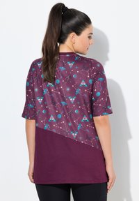 T-shirt à manches courtes en bordeaux foncé avec un haut à motifs présentant des yeux turquoise, des formes géométriques et des motifs célestes ; texture lisse.