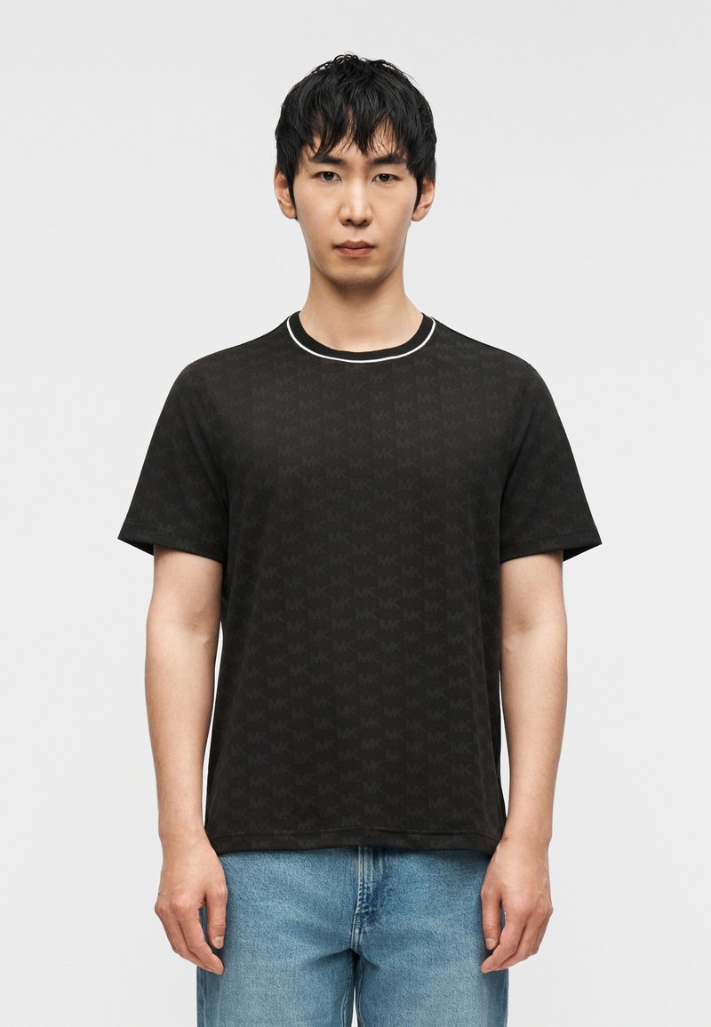 Μαύρο t-shirt με διακριτικό μοτίβο λογότυπου, κοντά μανίκια και στρογγυλή λαιμόκοψη με λευκή επένδυση, συνδυασμένο με μπλε τζιν παντελόνι.