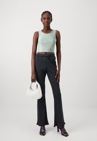 Lys grønn ribbet crop top, mørke stripete vidbukser, hvit quiltet håndveske og lilla høyhælte sandaler. Enkel, moderne design.