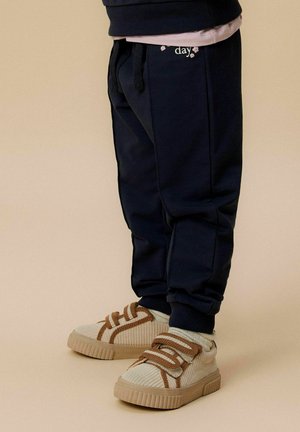 Granatowe dresy z elastycznym pasem i kieszeniami bocznymi, zestawione z beżowymi sneakersami z kordurowej tkaniny, posiadającymi brązowe sznurówki i teksturowane akcenty.