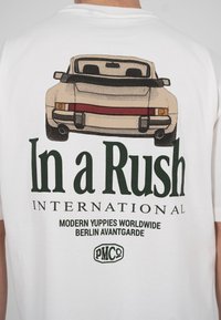 Illustrasjon av baksiden på en vintagebil med teksten "In a Rush", "International" og "Modern Yuppies Worldwide Berlin Avantgarde" på en hvit skjorte.