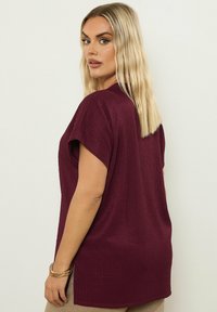 Bordowy top z krótkim rękawem o teksturowanym prążkowanym wzorze, w luźnym fasonie i z bocznymi rozporkami, pokazany z tyłu na jednolitym tle.