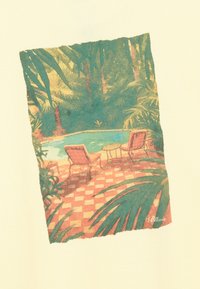 Deux chaises longues vides et une petite table ronde à côté d'une piscine, entourées de plantes et d'arbres tropicaux denses.