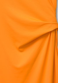 Tissu en coton orange au toucher doux, présentant une drape fluide et un détail torsadé sur un côté.