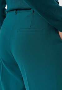 Spodnie w kolorze morskim o gładkiej fakturze, wąskim kroju, z szlufkami na pasek oraz dwoma tylnymi kieszeniami wykończonymi czystym przeszyciem.