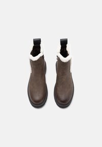 Botas de cuero marrón hasta el tobillo con suelas gruesas negras, forro de forro polar blanco alrededor de la abertura y tiradores negros en la parte trasera.