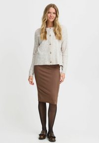 Cardigan gris clair à boutons avec une finition texturée, associé à une jupe crayon côtelée marron et des collants noirs. Des mocassins marron complètent le look.