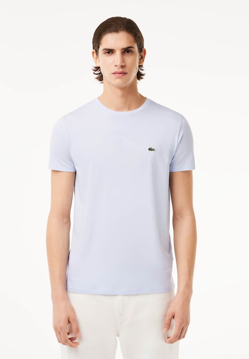 Camiseta de manga corta azul claro hecha de algodón suave, con un pequeño logo verde bordado en el pecho y un cuello redondo.