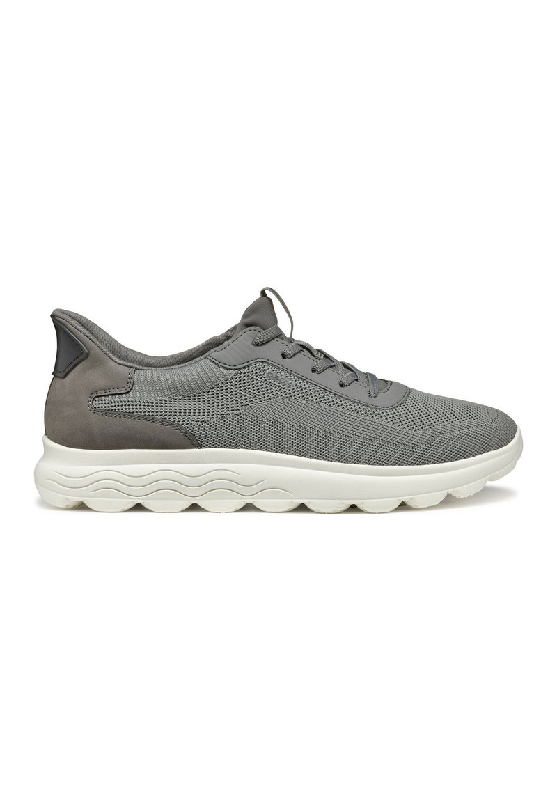 Sneaker grigia in rete con tallone in pelle scamosciata, lacci rotondi e una suola bianca testurizzata con motivi ondulati. Design traspirante per il comfort.
