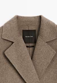 Bruine wolmix jas met een notch-kraag, voorzien van een label met de tekst "Massimo Dutti." Zachte textuur en minimalistisch ontwerp.