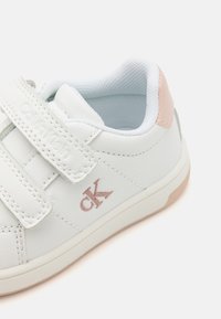Białe skórzane sneakersy z rzepami. Posiadają jasnoróżowy akcent na pięcie oraz metaliczne różowe logo z boku. Teksturowana powierzchnia.