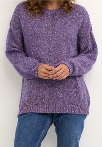 Lila stickad tröja med lös passform, med ett strukturerat, flerfärgat mönster och ribbade ärmar, som bärs tillsammans med blå jeans.