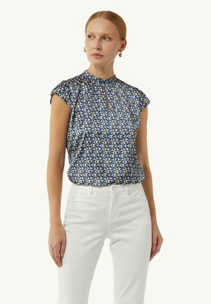 Blue patterned blouse with short, puffed sleeves, pleated neckline, and keyhole detail, paired with white pants. Smooth fabric, geometric design.
