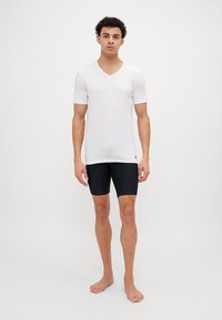 T-shirt blanc à manches courtes et col en V associé à un short noir ajusté, tous deux en tissu extensible, avec un minimum de marquage sur le T-shirt.