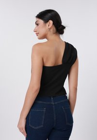 Μαύρο τοπ με έναν ώμο και σκουφάκι στη ραφή του ώμου, συνδυασμένο με σκούρα μπλε τζιν τζιν που διαθέτει πίσω τσέπες και εφαρμοστή σχεδίαση.