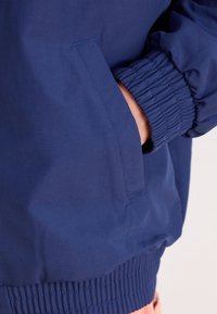 Mörkblå bomberjacka med elastiska muddar, sidficka och ett smidigt, lätt material. Designad med en avslappnad passform.