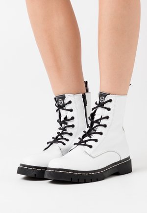 Stivaletti alla caviglia in pelle bianca con lacci neri, suola spessa nera e cuciture decorative. Presentano una cerniera laterale e un dettaglio con logo sulla linguetta.