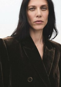 Blazer de terciopelo marrón de doble botonadura con solapas de pico y botones grandes, que presenta una textura suave y una silueta estructurada.