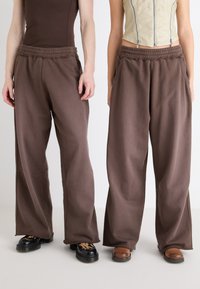 Braune weite Sweatpants mit elastischem Bund und Seitentaschen, aus weichem Stoff mit glatter Textur gefertigt.