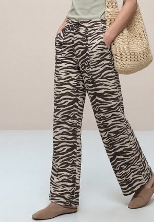 Persoon draagt een wijde zebra-print broek, beige instapschoenen en draagt een grote beige gehaakte tote tas op de schouder.
