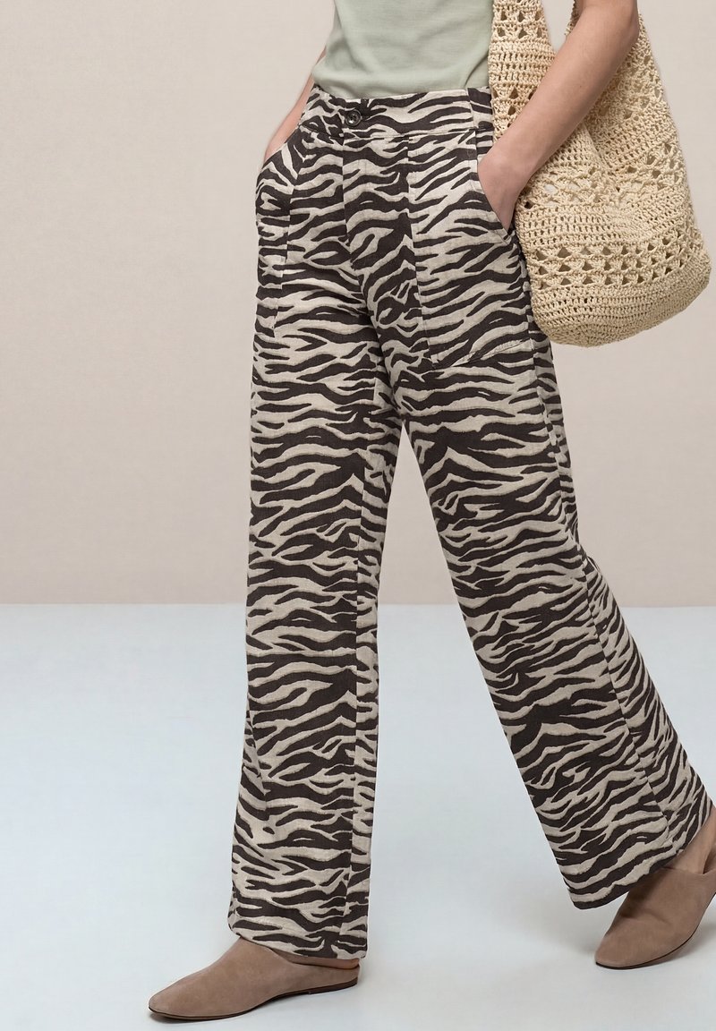 Personne portant un pantalon large à imprimé zèbre, des chaussures beige sans lacets, et portant un grand sac cabas beige en crochet sur l'épaule.