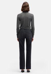 Szary dopasowany sweter z wysokim kołnierzem, połączony z ciemnoszarymi jeansami o prostych nogawkach. Gładka tekstura, delikatne przeszycia i klasyczny design tylnych kieszeni.