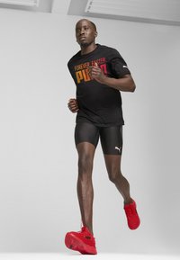 Camiseta de running negra con texto degradado "FOREVER FASTER. PUMA", combinada con pantalones cortos negros y zapatillas deportivas rojas con la marca Puma.