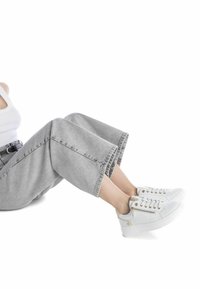 Zapatillas blancas con una textura suave, detalles en dorado y cordones. Combinadas con pantalones cortos y de pierna ancha en gris claro.