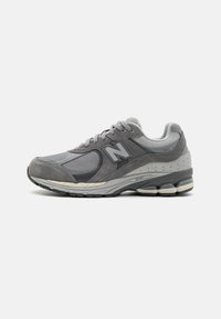 Chaussure de sport grise avec une tige en mesh et en daim, accents texturés, fermeture à lacets et semelle rembourrée avec des poches d'air visibles.