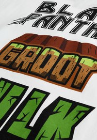 Fehér póló, élénk grafikával: a tetején "Fekete Párduc", "GROOT" barna fa textúrával, és "HULK" zöld, repedezett betűkkel.