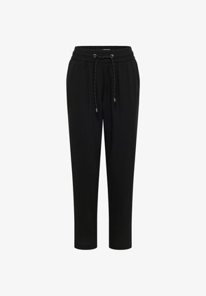 Femme portant une chemise bleu clair, un pantalon noir avec cordon, des sandales beiges, une casquette jaune, et un sac à bandoulière tissé beige.