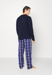 Herenset voor huismode met een marineblauwe longsleeve top en een blauwe geruite pyjamabroek. Kenmerkt zich door zacht materiaal en een losse pasvorm met een comfortabele tailleband.