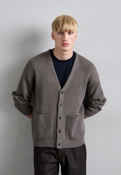 Grå räfflad cardigan med V-ringning, långa ärmar, två framfickor och knappstängning. Det texturerade stickade materialet ger djup åt designen.