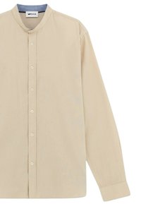 Camicia beige a maniche lunghe con colletto a band, chiusura frontale con bottoni e una texture liscia. Presenta una leggera lucentezza e un design minimalista.
