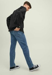Camisa negra de botones con jeans rectos azules y zapatillas negras. La camisa tiene mangas largas y botones a presión.