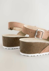 Sandales à plateforme en daim marron avec des brides de cheville ajustables, présentant une semelle de base en liège naturel et une semelle en caoutchouc blanche.