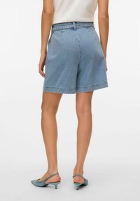 Šviesiai mėlynos džinsinės šortai, laisvo kirpimo, vidutinio aukščio juosmuo ir nebaigtas kraštas. Suderinti su žalsvai mėlynomis šlepetėmis ant kulno.