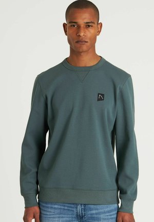 Sudadera verde hecha de tela texturizada con cuello redondo y puños acanalados. Presenta un parche de logo negro en el pecho izquierdo.