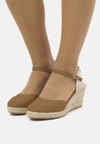 Scarpe con tacco in suede marrone, con suola in corda intrecciata, cinturino alla caviglia e dettaglio in tessuto testurizzato sul tacco. Design a punta arrotondata, finitura liscia.