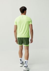 Kortärmad, neongrön träningsskjorta med texturerad tyg, ihop med mörkgröna shorts med en ljusgrön fåll. Vita strumpor med svarta ränder.