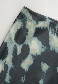 Black and teal animal print fabric featuring soft texture, irregular spots, and a smooth finish, with light green accents and a folded edge.