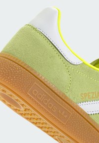 Gröna mockaskor med vita läderdetaljer, gula kanter och sula av gummi. Har texturerad yta och 'adidas'-logotyp.