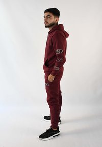 Sudadera burdeos y joggers a juego, hechos de tela con detalles de logotipo bordado. Complementados con zapatillas deportivas negras. Diseño simple y deportivo.
