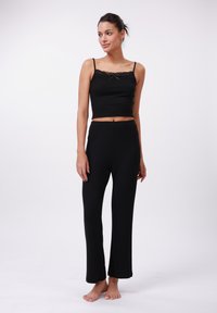 Černá dvoudílná souprava na volný čas obsahující přiléhavý, cropped top s krajkovými detaily a nastavovacími ramínky, doplněná o volné kalhoty rovného střihu.