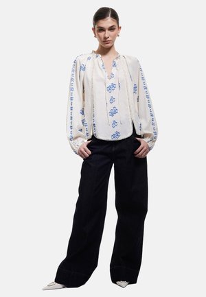Hvid bluse med blå blomsterbroderi, sammensamlet halsudskæring og lange ærmer. Kombinationen med sorte vide bukser og spidse hvide sko.