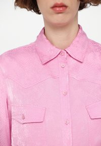 Pink, textured button-up shirt with a snake-skin pattern, featuring a collar and two chest pockets.
