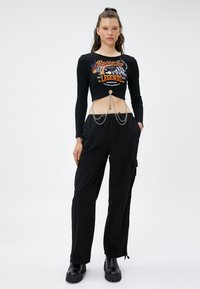 Zwart geribbeld crop top met grafische print en kettingdetail, gecombineerd met losse zwarte cargobroek en chunky zwarte platformlaarzen.