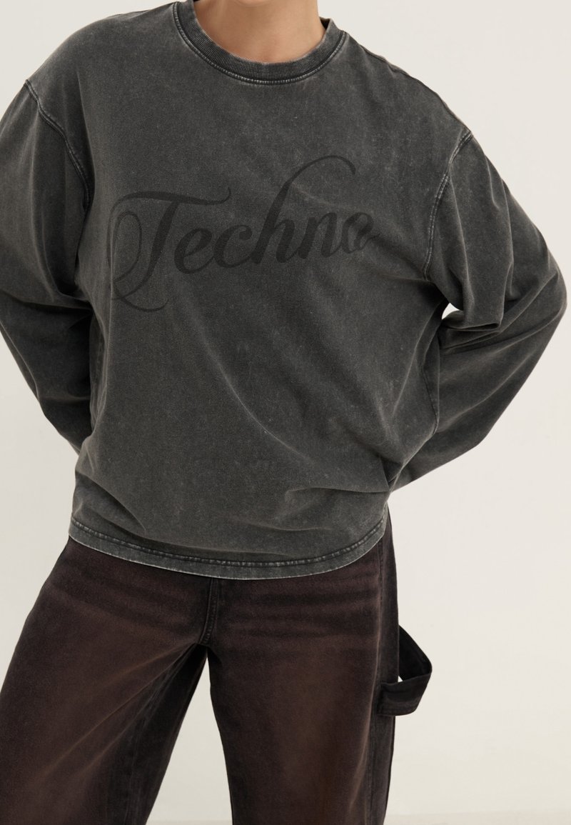 Musta huppari, jossa on iso "Techne"-teksti kirjoitettuna. Hupparissa on rento istuvuus, pyöreä kaula-aukko ja hieman kulunut pinta.